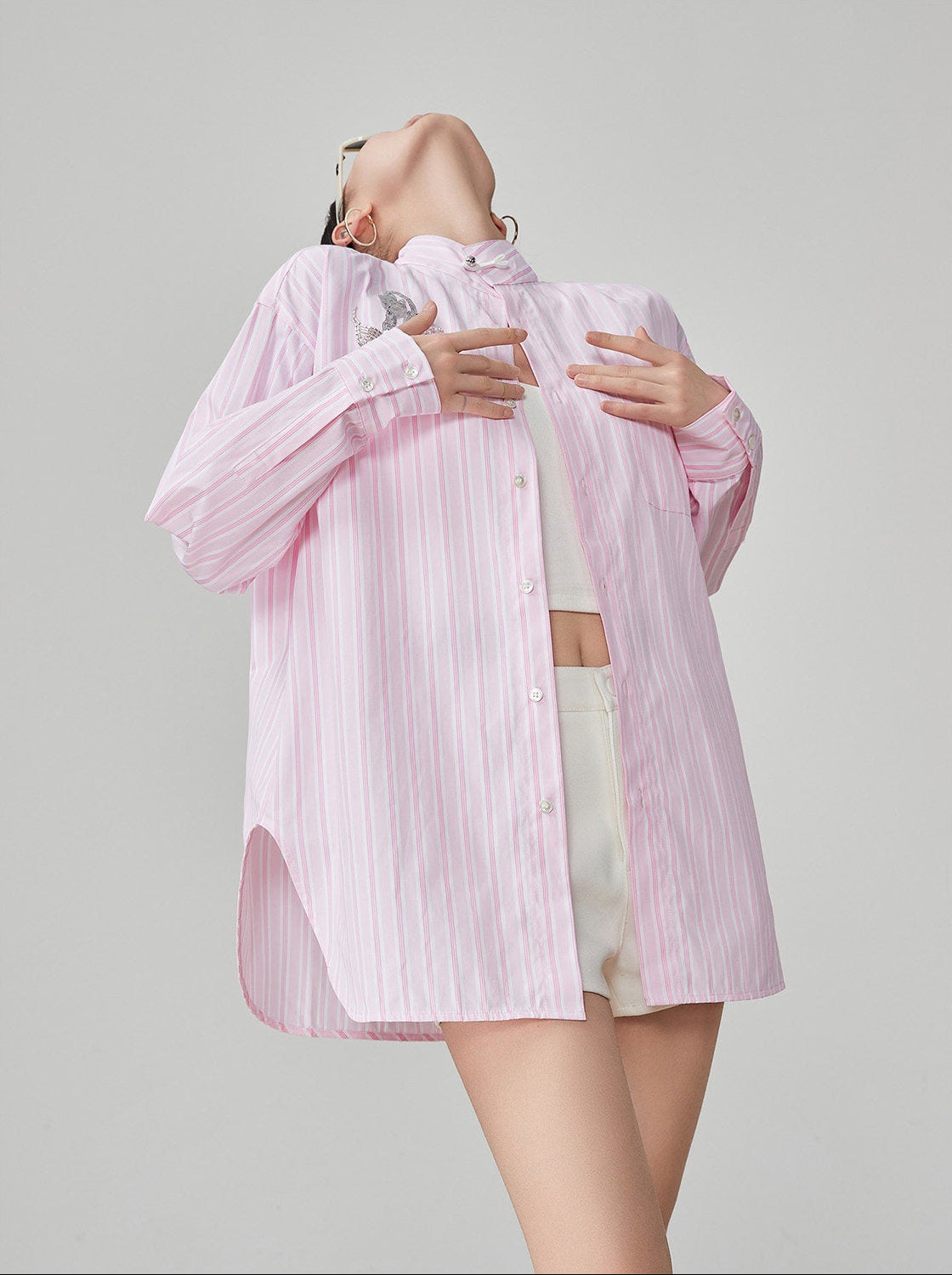 Person wearing a light pink striped shirt over a white top and light shorts on a gray background