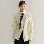 Woman wearing a white blouse with black polka dots and a black bow tie against a plain background