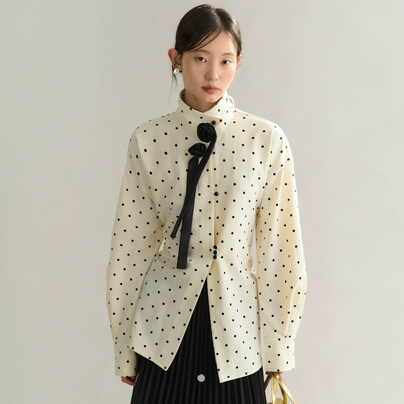 Woman wearing a white blouse with black polka dots and a black bow tie against a plain background