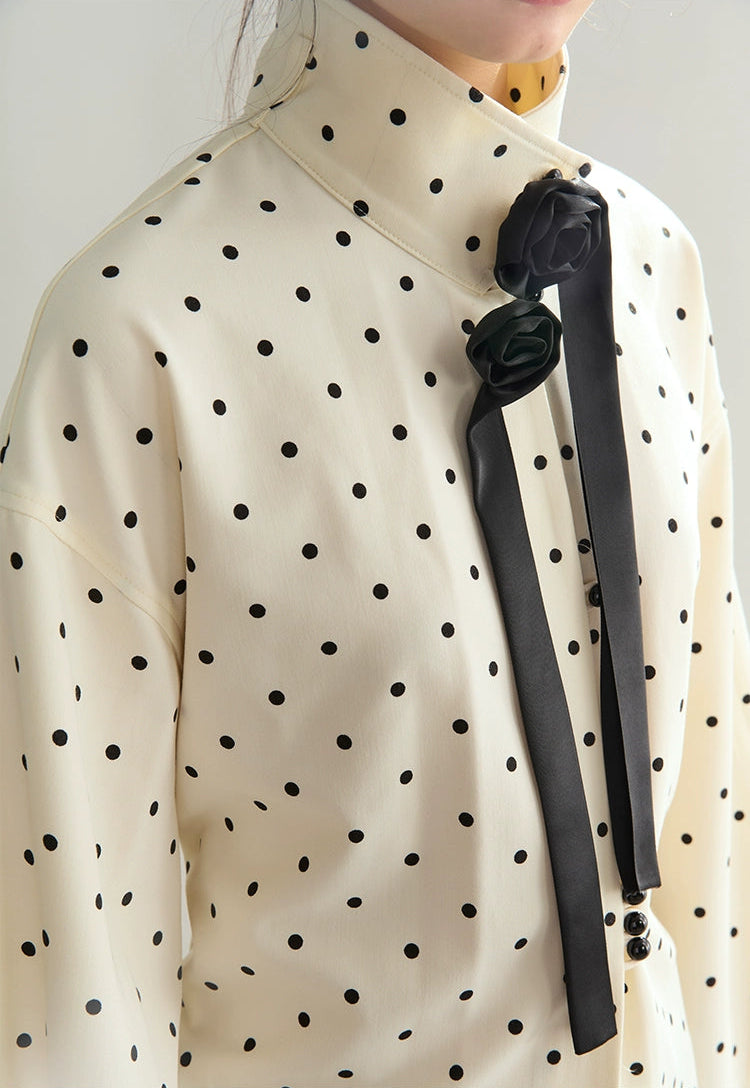White blouse with black polka dots and a black bow tie on a plain background