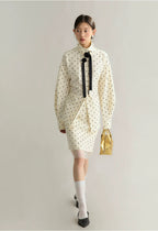 Woman wearing a white polka dot dress with a black bow tie on a plain background