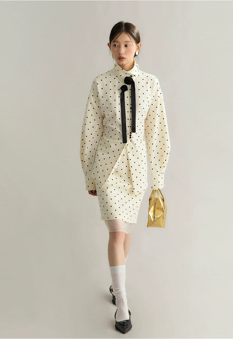 Woman wearing a white polka dot dress with a black bow tie on a plain background