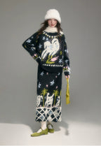 Woman wearing a black patterned sweater and skirt with a white hat on a gray background