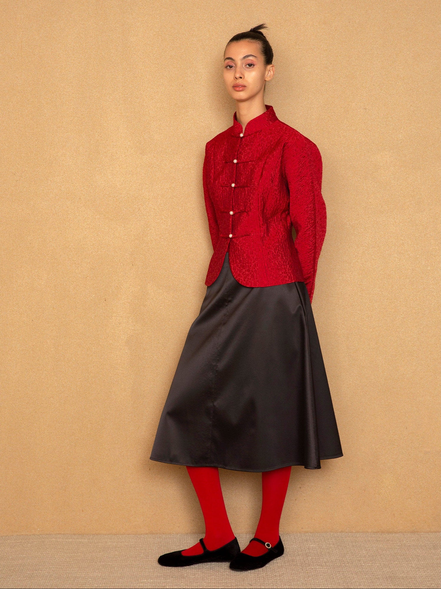 Person wearing a red jacket and black skirt against a beige background