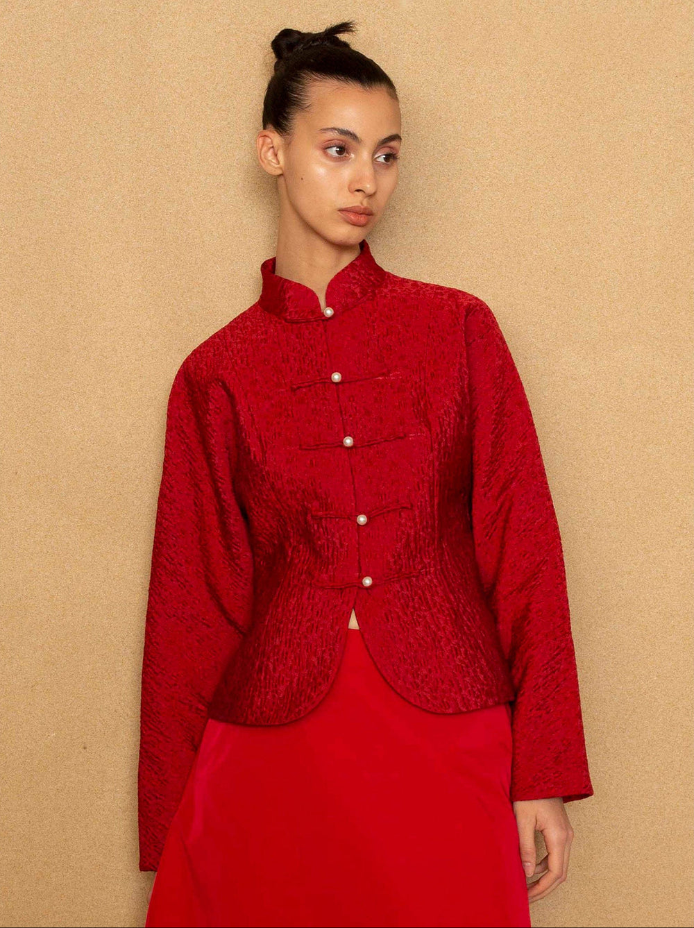 Woman wearing a red jacket and skirt against a beige background