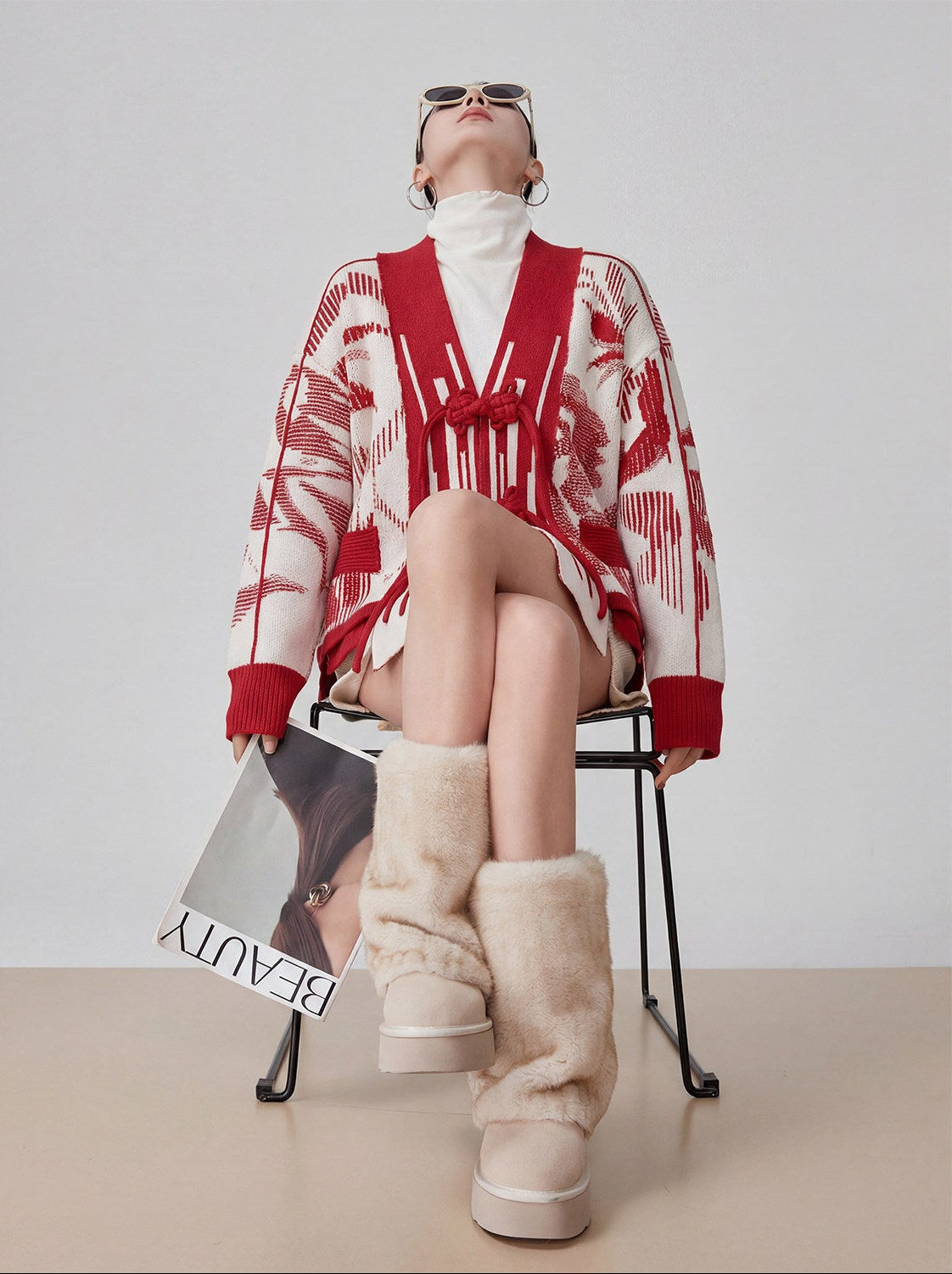 Person wearing a red and white patterned cardigan and beige boots, holding a magazine titled 'Beauty'.