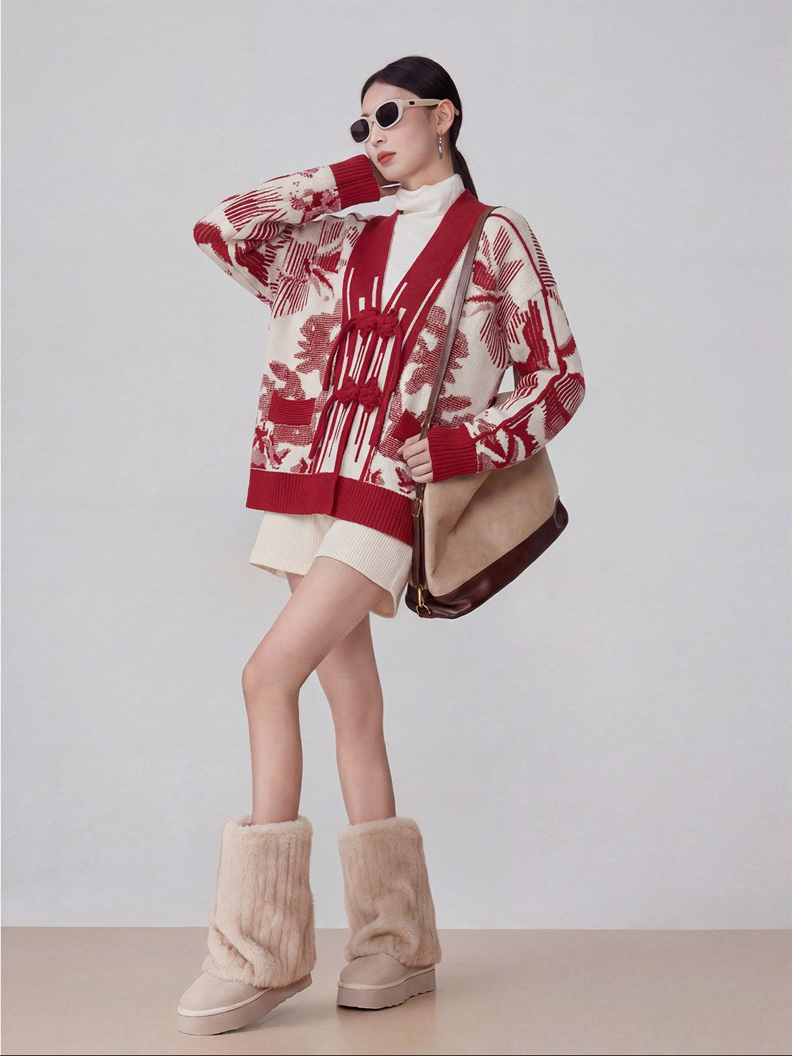 Person wearing a red and white patterned cardigan with beige boots on a plain background