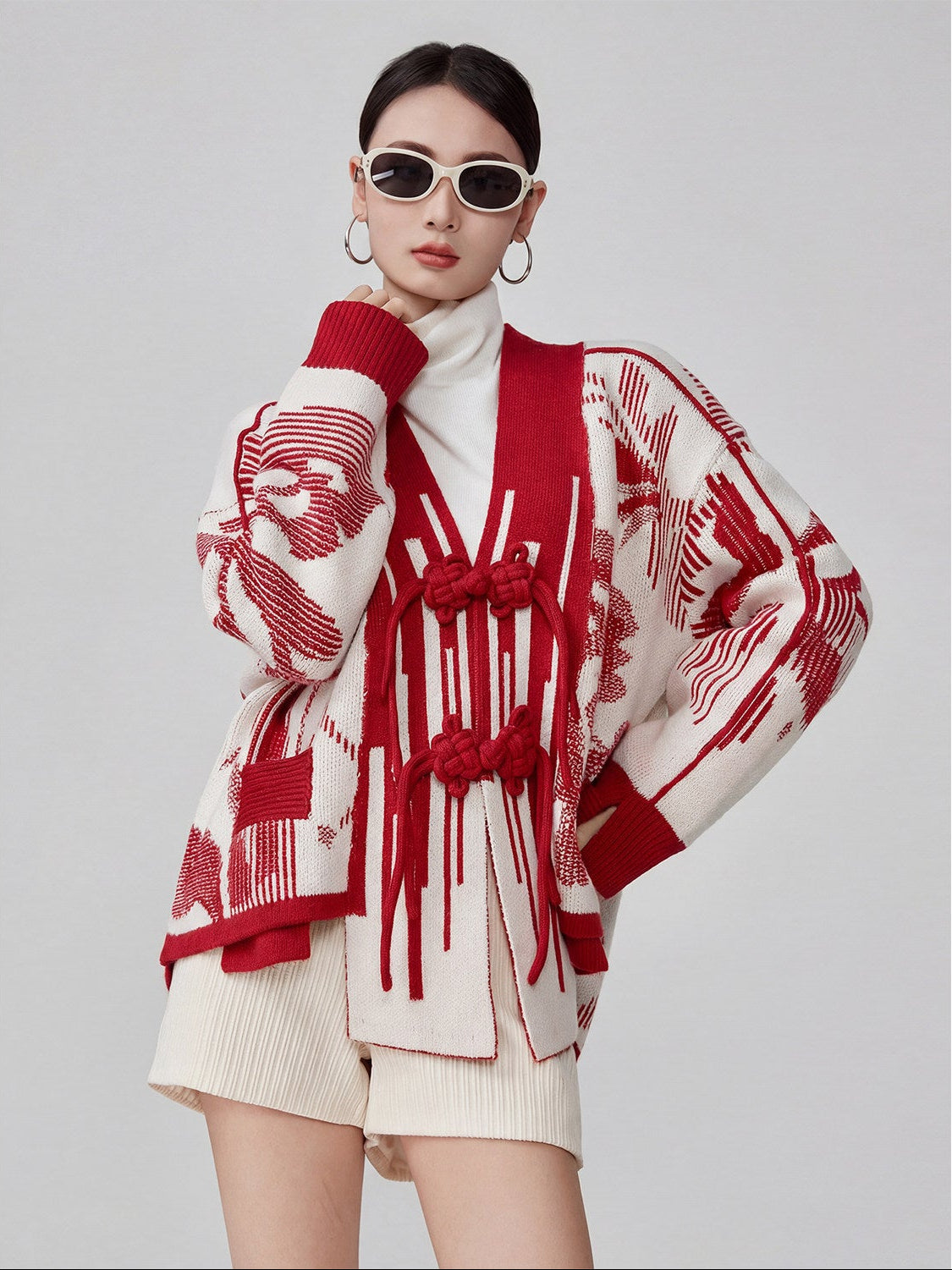 Woman wearing a red and white patterned sweater over a white outfit on a gray background