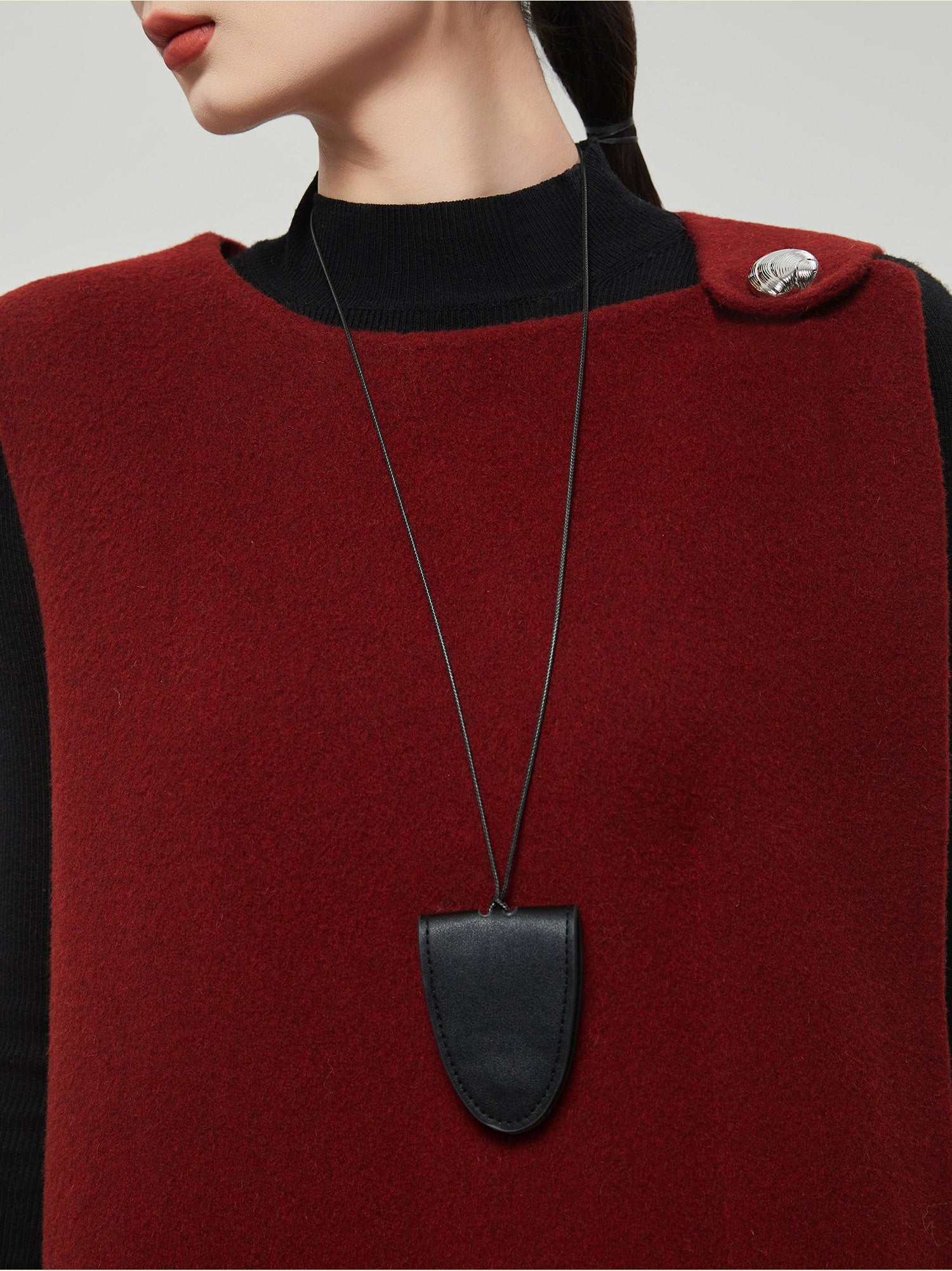 Person wearing a red garment with a black necklace featuring a shield-shaped pendant.