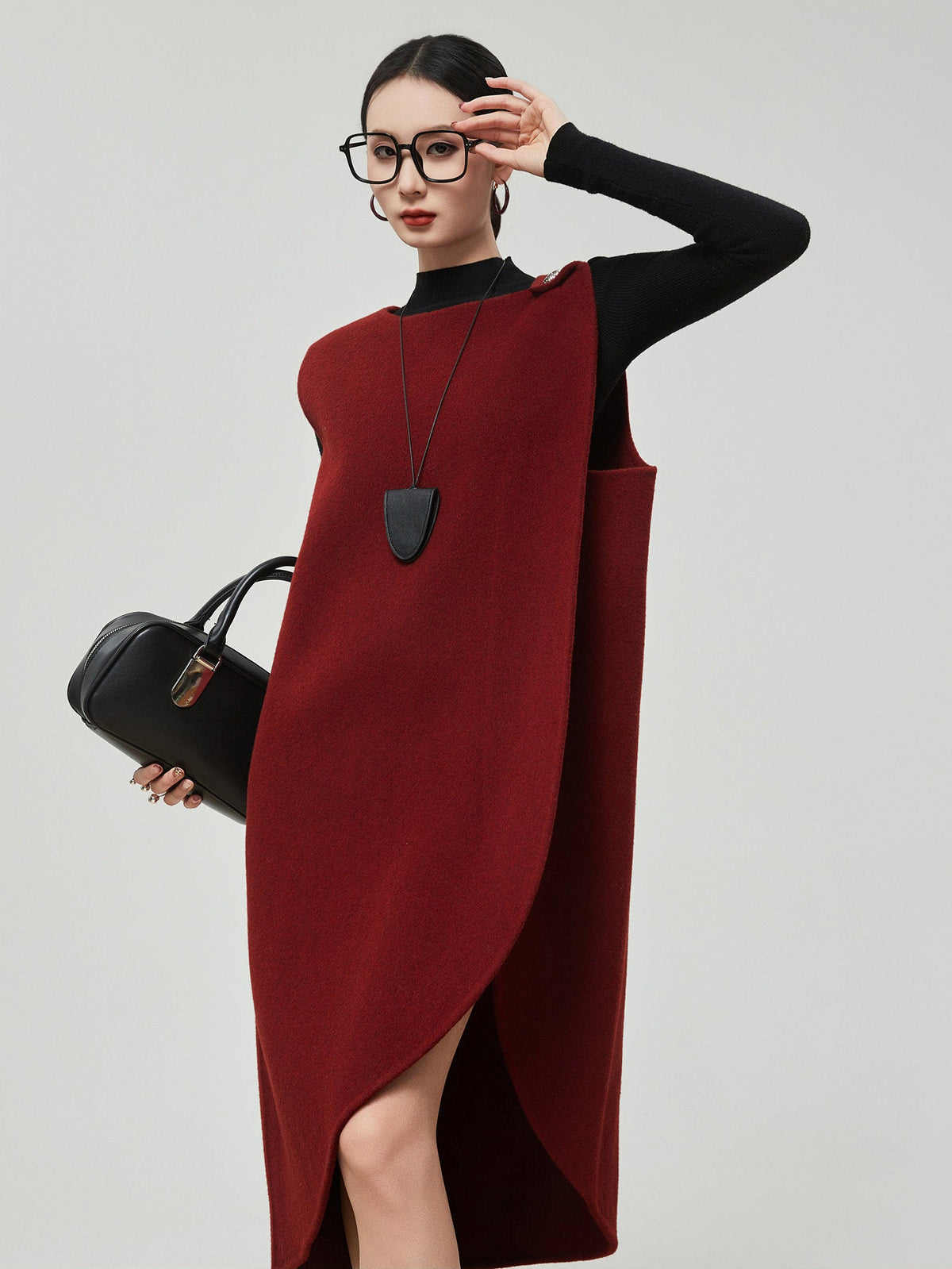 Woman wearing a red dress with a black top and holding a black handbag on a light gray background