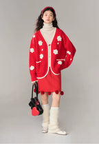 Person wearing a red cardigan with white floral patterns, a matching skirt, white turtleneck, and knee-high socks, holding a black handbag.