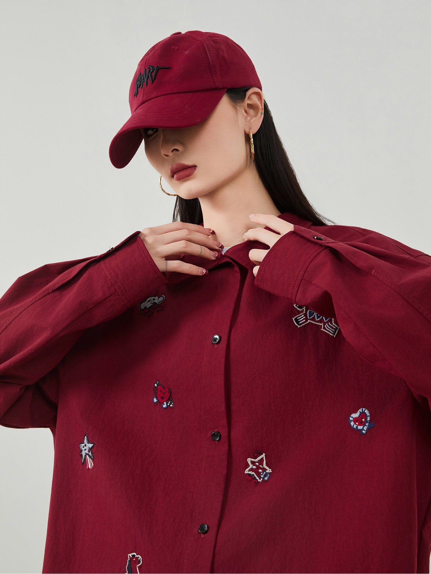 Person wearing a red embroidered shirt and cap against a gray background