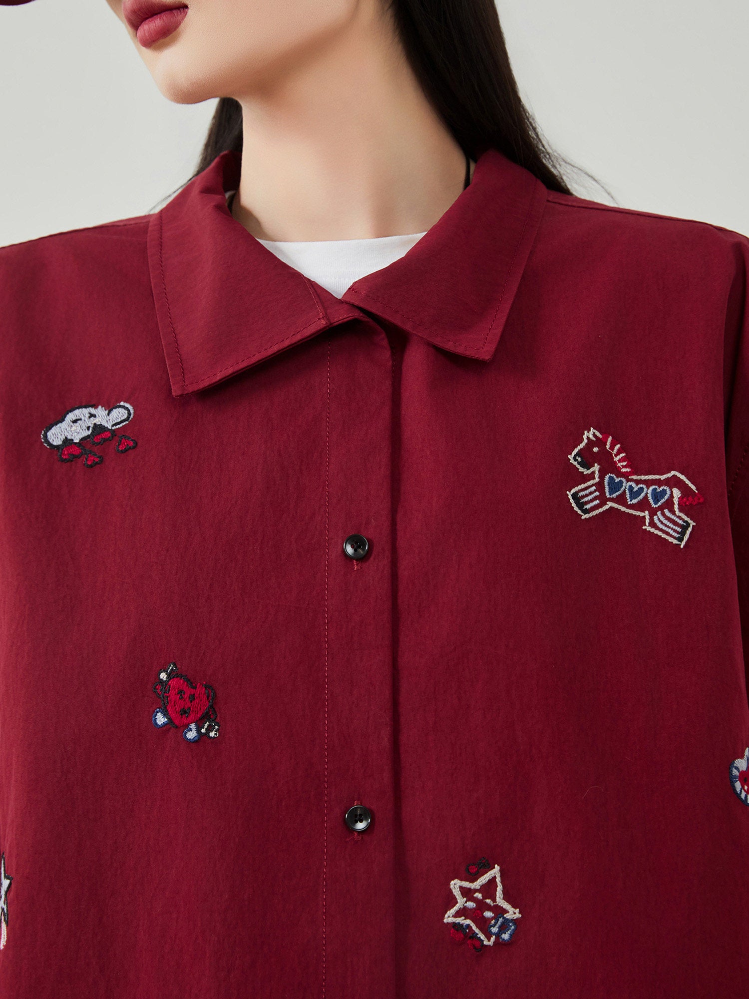 Close-up of a maroon shirt with embroidered designs on a plain background