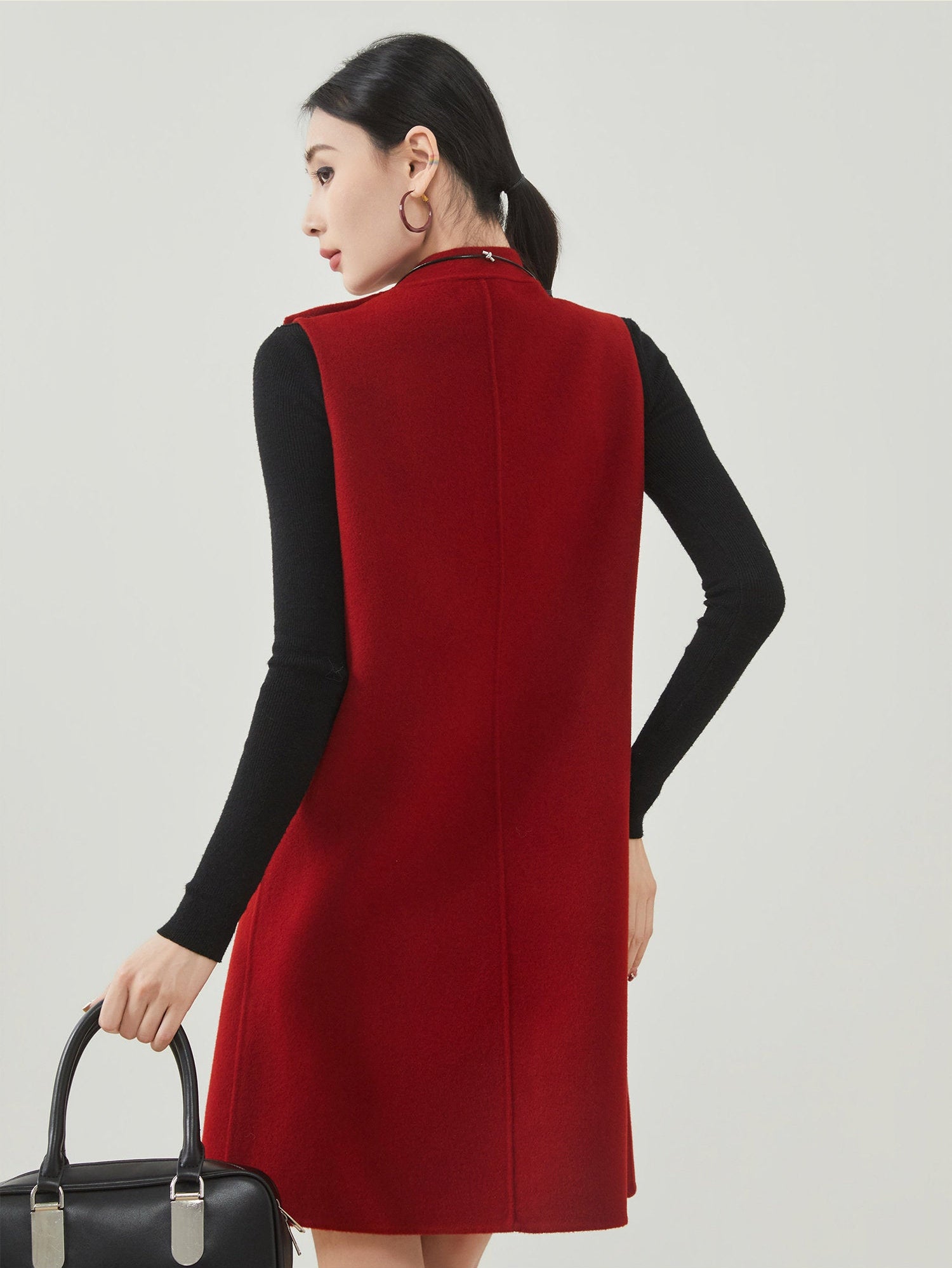 Woman wearing a red sleeveless dress over a black long-sleeve shirt on a light gray background