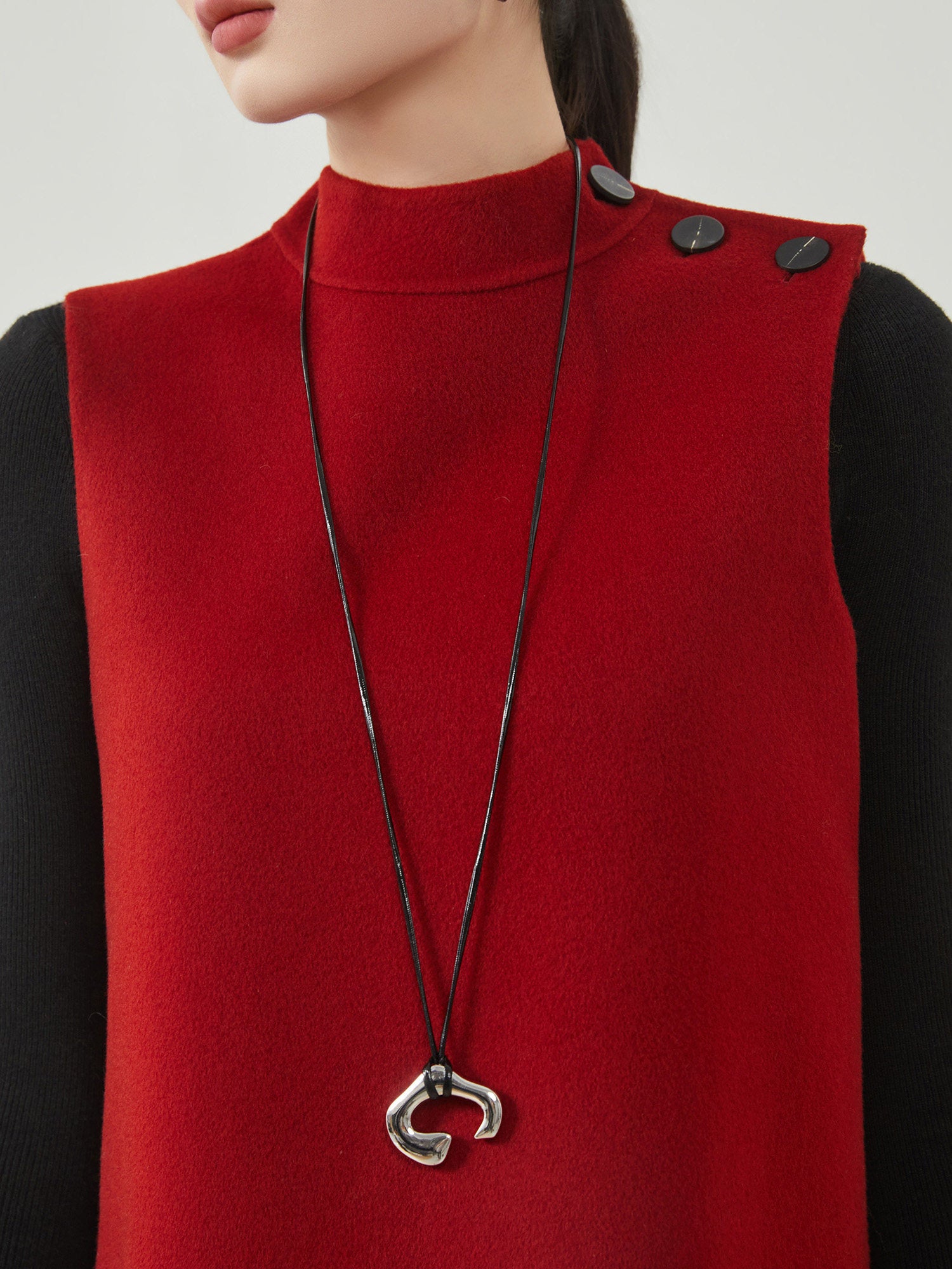 Person wearing a red vest with a black necklace featuring a silver pendant.