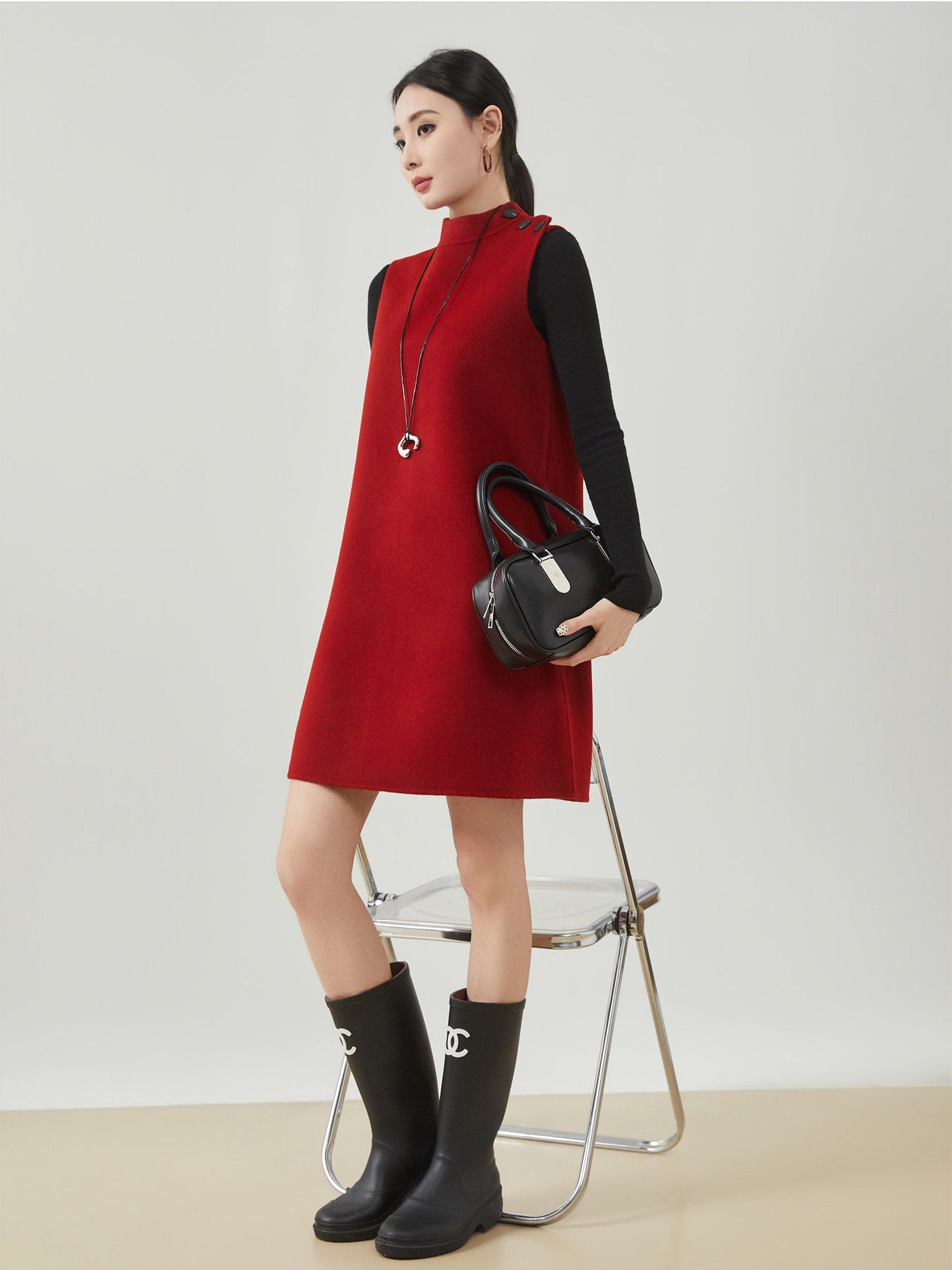 Woman wearing a red dress and black rain boots holding a black handbag on a white background