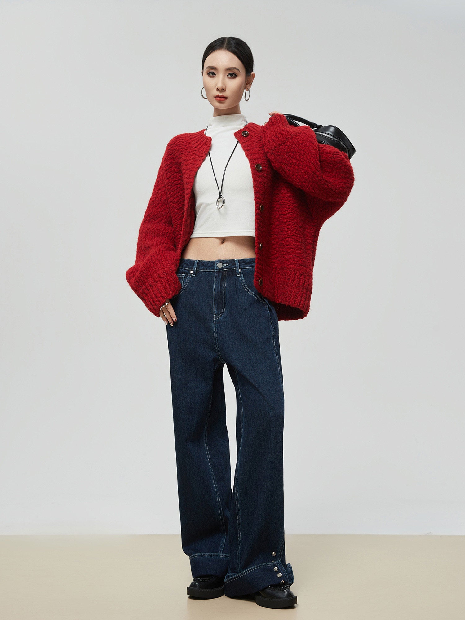 Woman wearing a red cardigan, white top, and blue jeans on a plain background