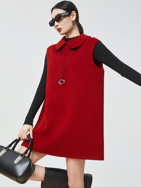 Woman wearing a red sleeveless dress with a black top, holding a black handbag on a white background.