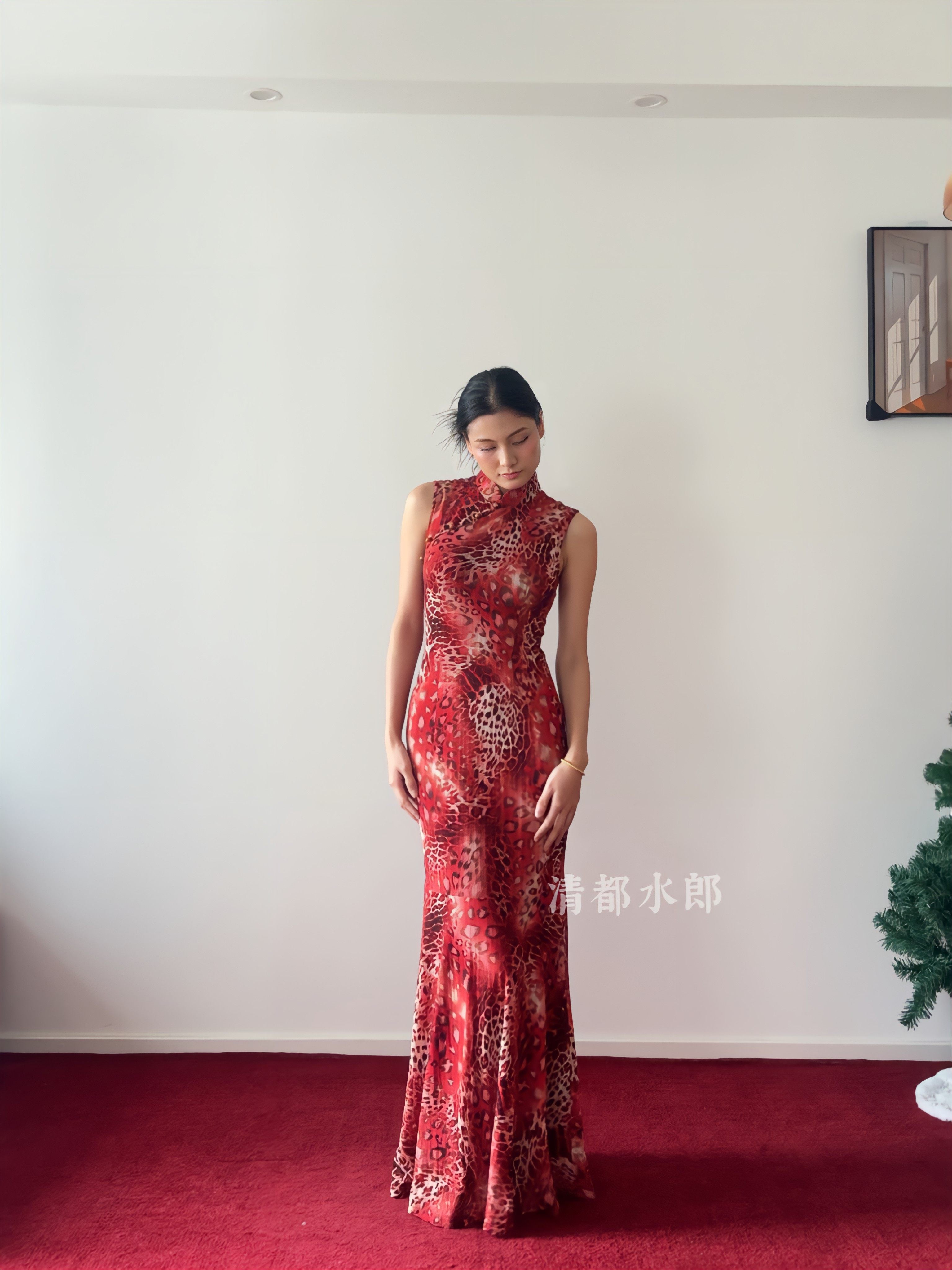 Woman wearing a red patterned dress standing on a red carpet with a white wall background.