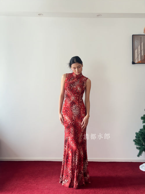 Woman wearing a red patterned dress standing on a red carpet with a white wall background.