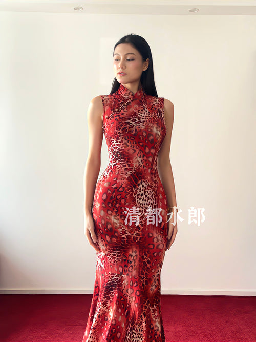 Woman wearing a red and black patterned dress against a white wall.