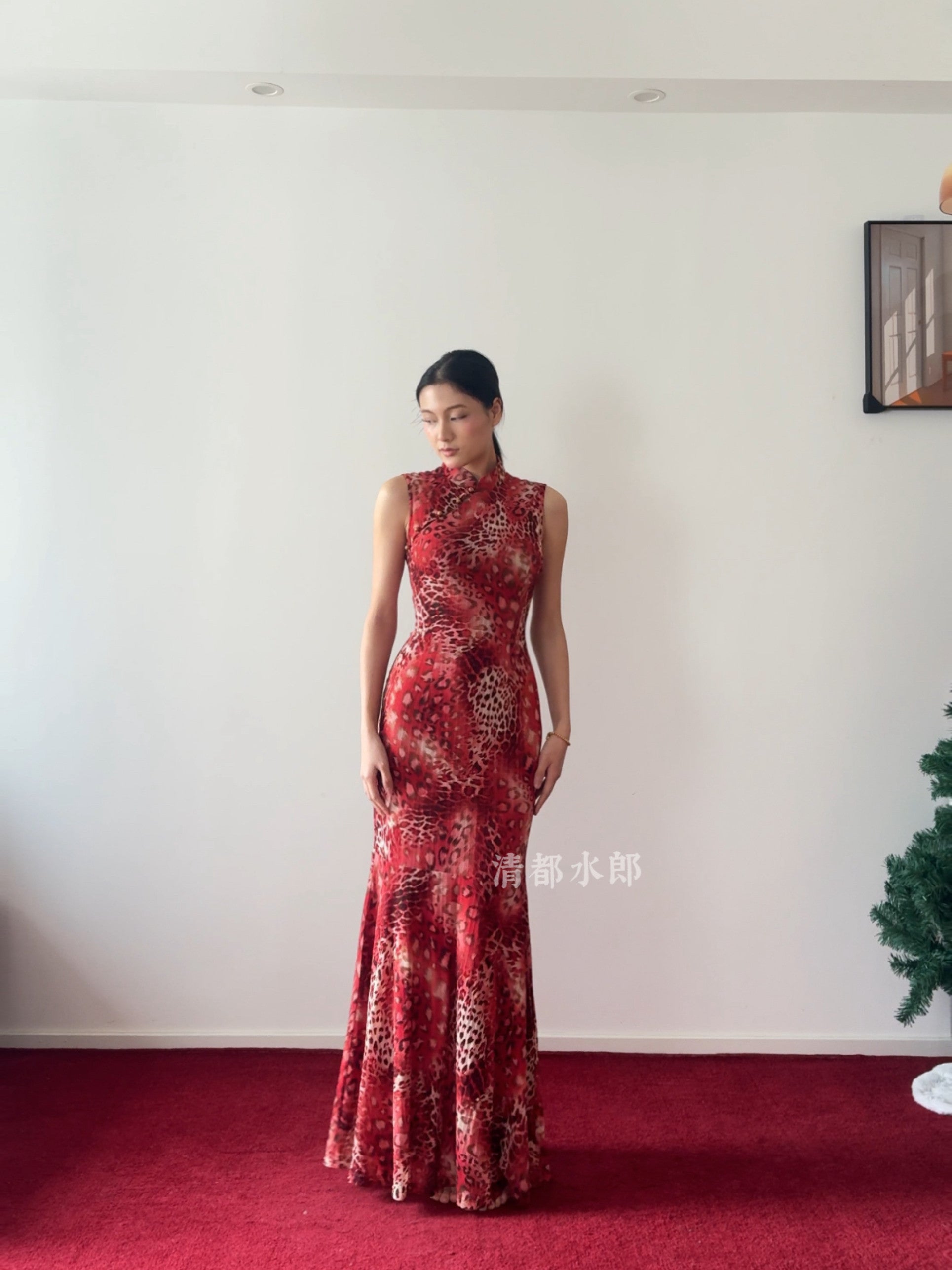Woman wearing a red floral dress standing against a white wall.