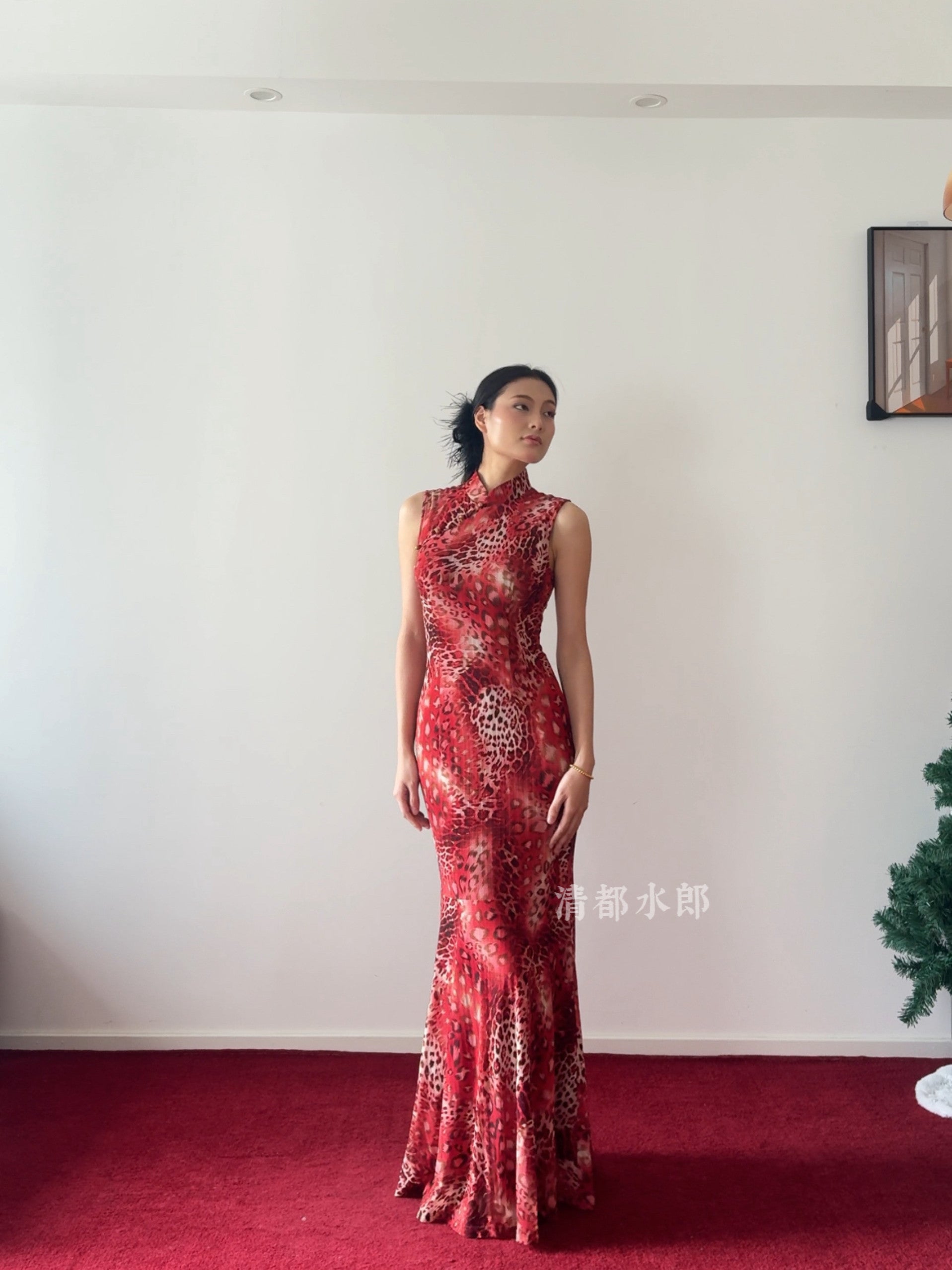 Woman in a red patterned dress standing on a red carpet with a white wall background