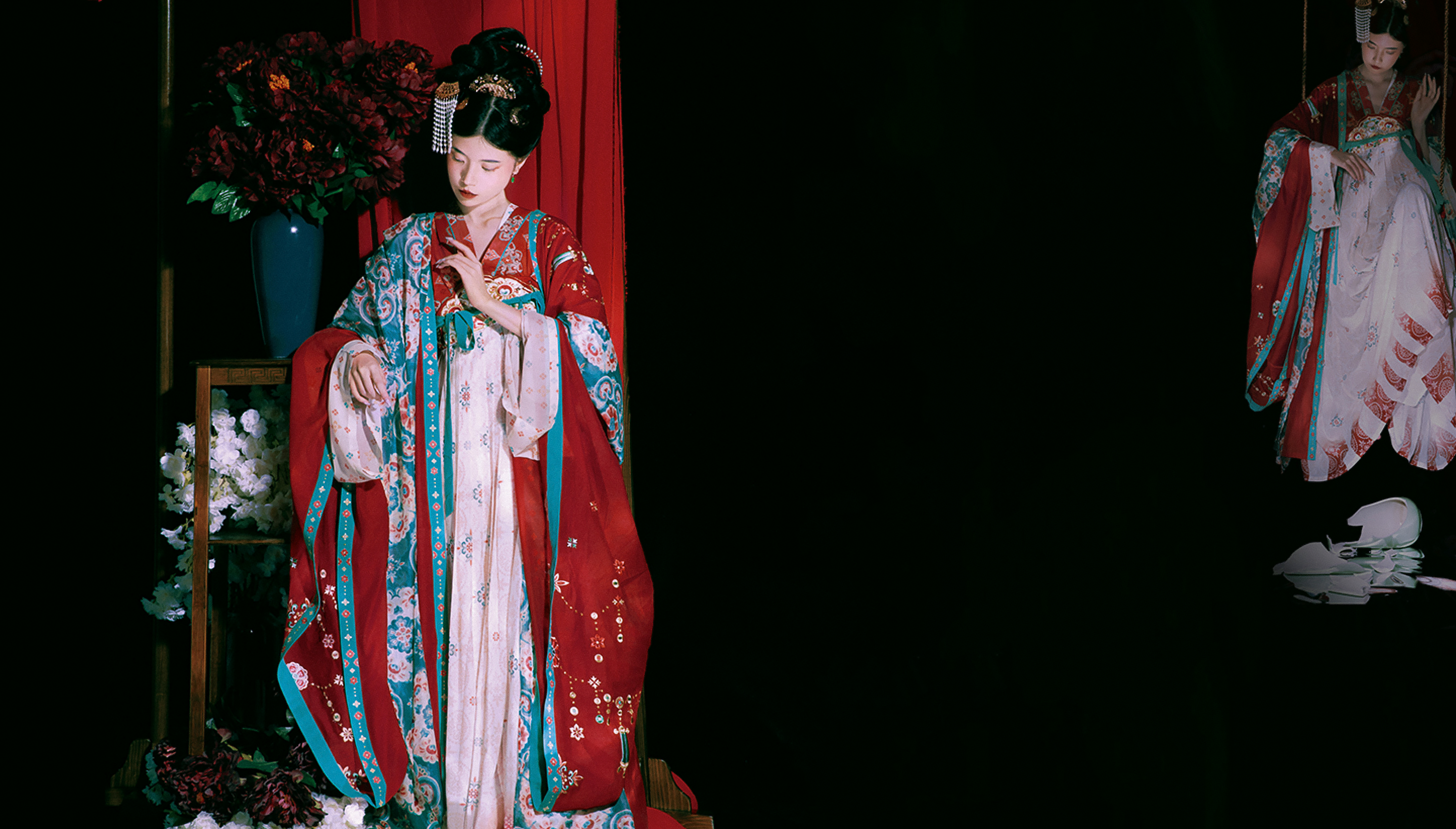 Woman in red and white patterned hanfu near flowers and a red curtain. 
