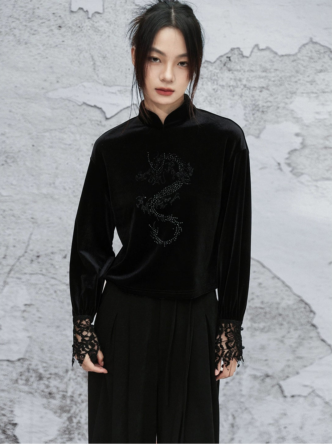 Person wearing a black outfit with lace details against a textured wall.