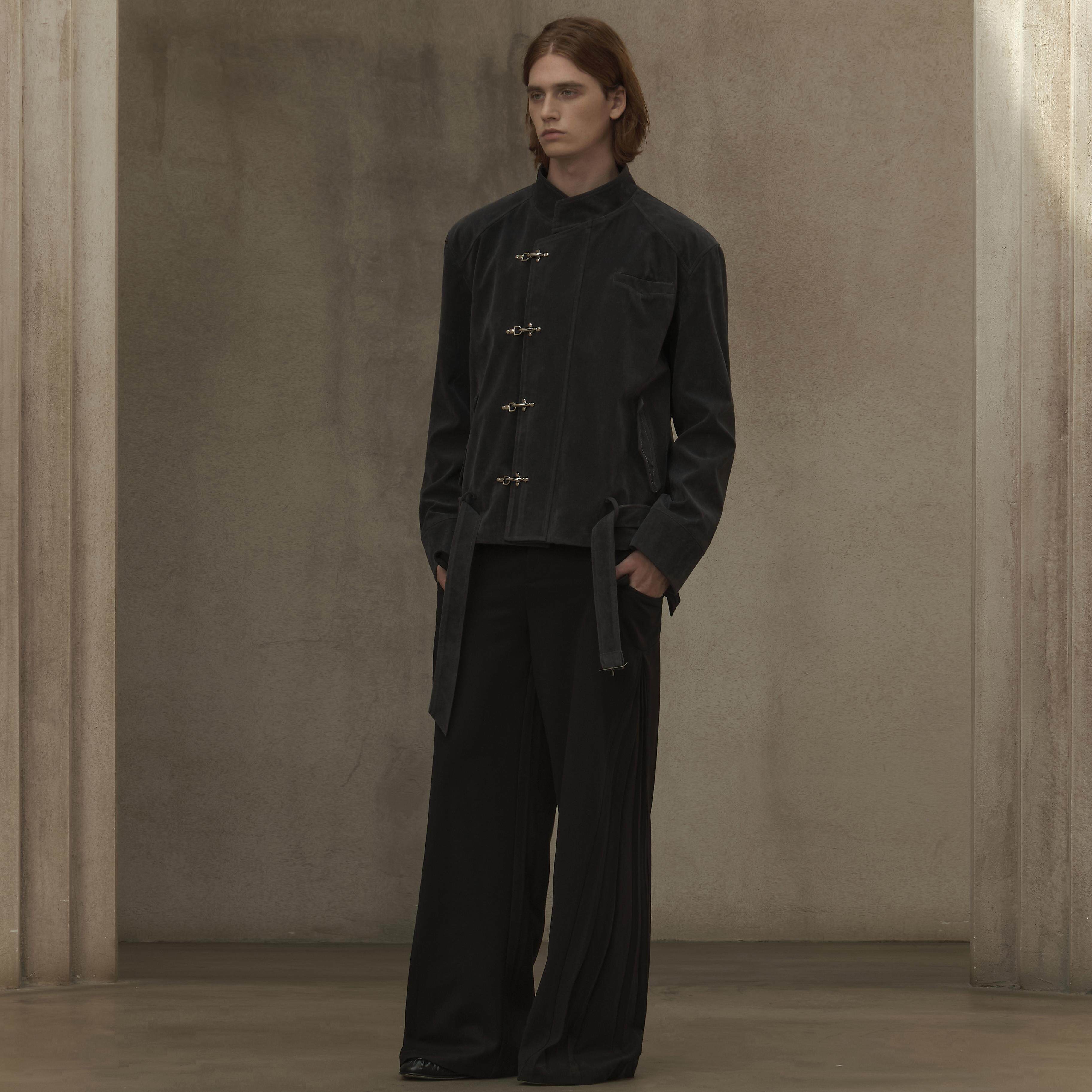 Person wearing a black outfit standing against a plain wall.