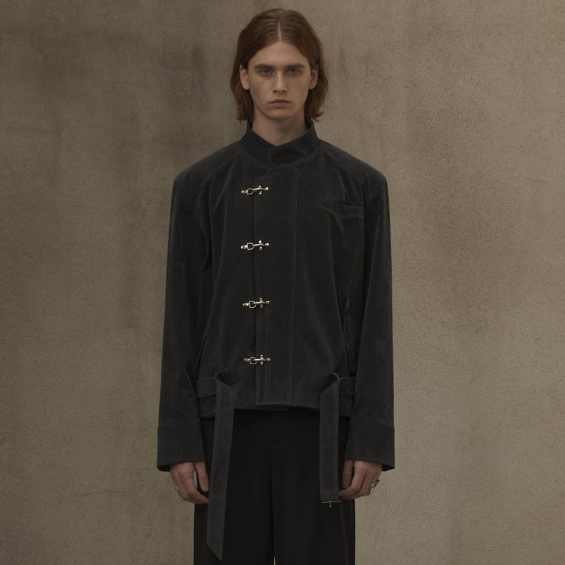 Person wearing a black outfit with button details against a brown background