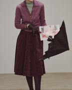 Woman wearing a purple coat and holding a black umbrella against a plain background