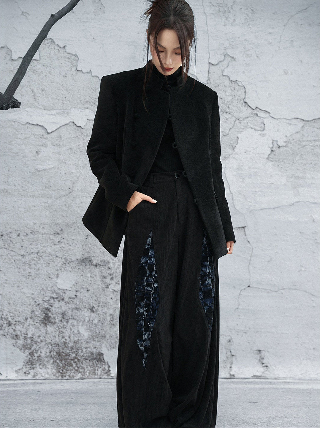 woman standing wearing a velvet suit jacket against a grey background.  