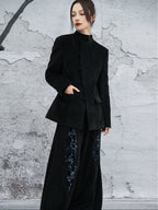 woman standing wearing a velvet suit jacket against a grey background. 