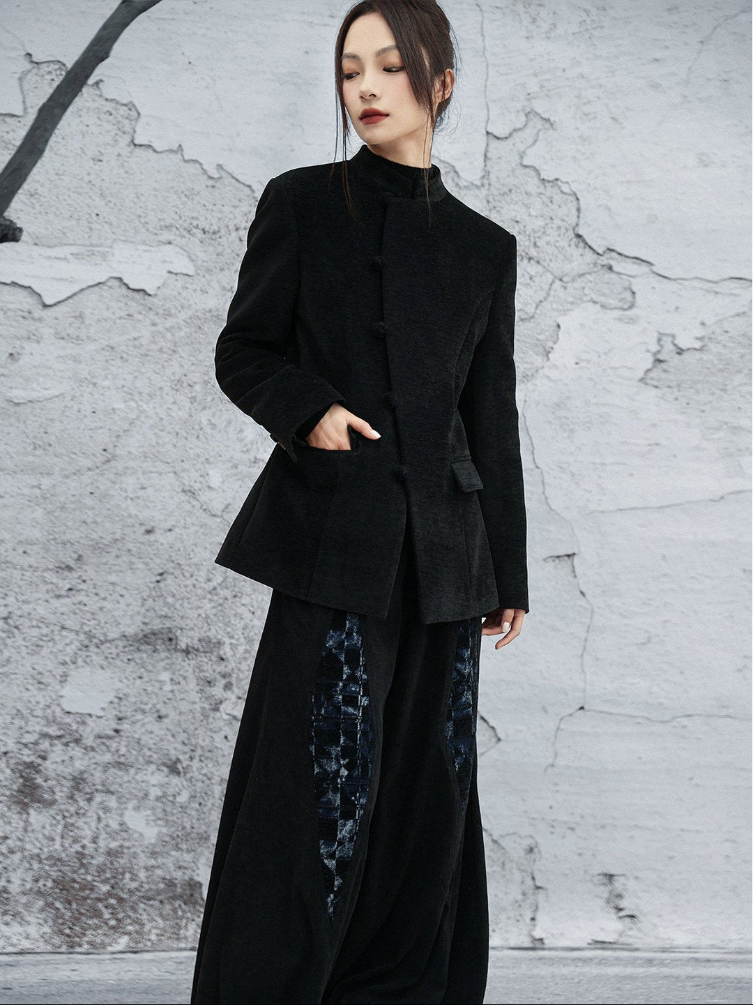 woman standing wearing a velvet suit jacket against a grey background. 