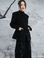 woman standing wearing a velvet suit jacket against a grey background. 