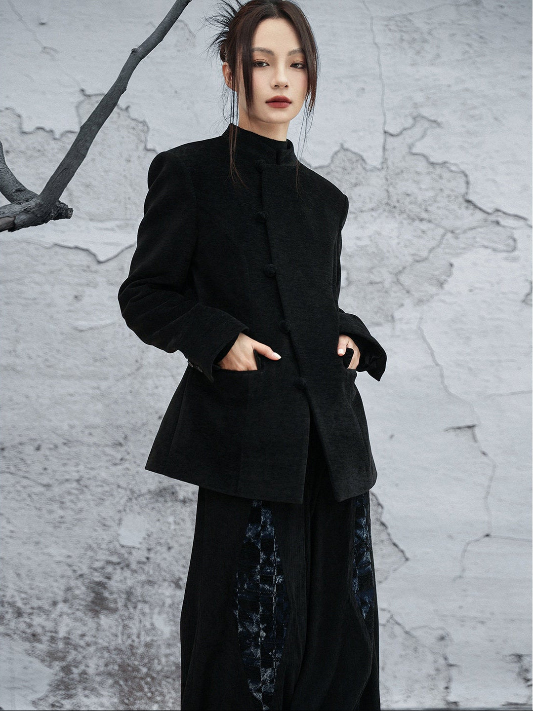 woman standing wearing a velvet suit jacket against a grey background. 