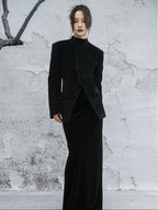 woman standing wearing a velvet suit jacket against a grey background.  