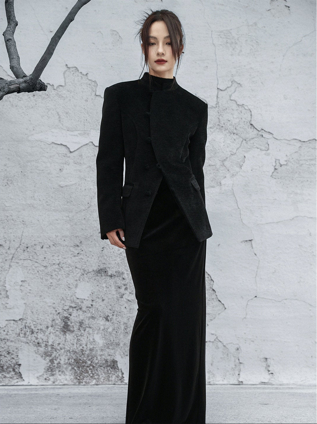 woman standing wearing a velvet suit jacket against a grey background.  