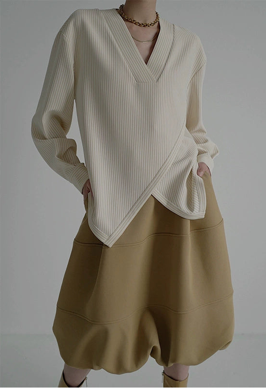 Person wearing a cream sweater and beige skirt on a gray background