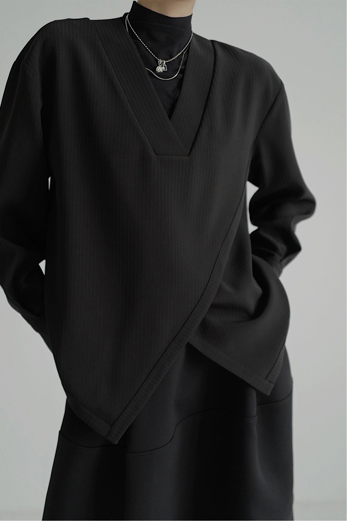 Black outfit with a V-neck top and long sleeves on a gray background