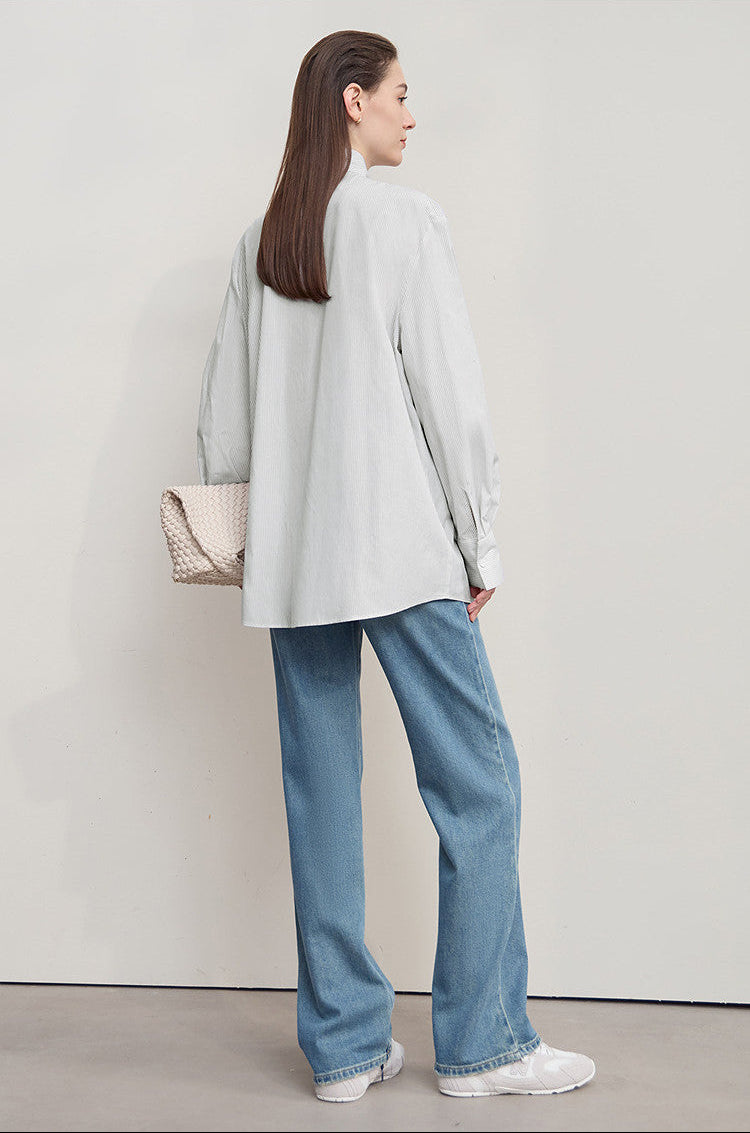 Woman wearing a light gray coat and blue jeans, standing against a plain background