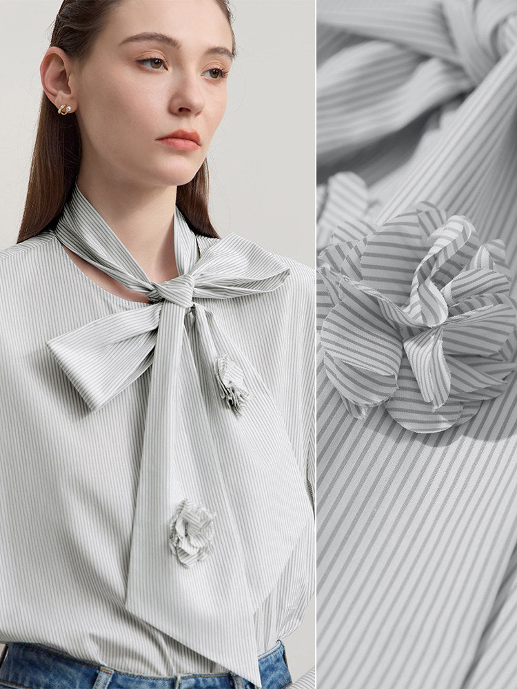 A woman wears a light gray and white vertically striped blouse with a large bow at the neckline and matching fabric flower appliqués. The image includes a close-up inset of the blouse fabric and bow detail on the right.