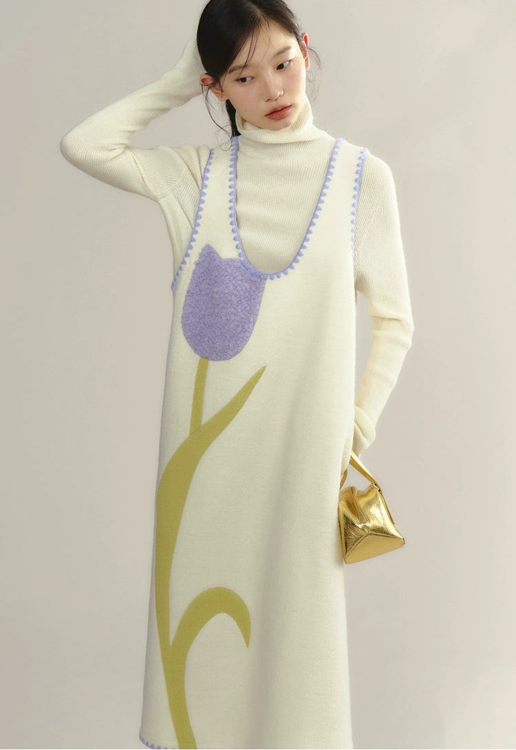 Woman wearing a long cream dress with a tree design, holding a gold handbag.