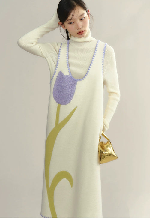 Woman wearing a long cream dress with a tree design, holding a gold handbag.