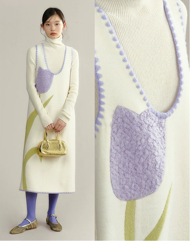 Woman wearing a long cream sweater with a purple floral pattern, holding a gold handbag.