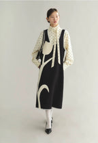 Woman wearing a black and white dress with a polka dot blouse on a light gray background