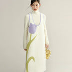 Woman wearing a long, cream-colored dress with a purple floral pattern on a plain background