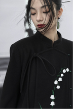 Person wearing a black coat with white floral embroidery on a plain background