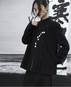 Person wearing a black coat with white floral embroidery against a blurred background